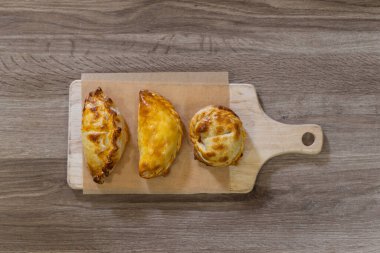 Parşömen kağıdının üzerine tahta bir kesme tahtasının üzerine çıtır çıtır kabuklu üç altın sarısı börek. Rustik tahta tablo arkaplanı, tepeden tırnağa görünüm, kopyalama alanı ile basit bir sunum.