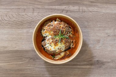 Doldurulmuş patlıcanla doldurulmuş patlıcan ve zengin bir domates sosunun içinde oturan eko-dost bir yemek kasesinde servis edilen gurme yemeğinin genel görüntüsü. Kopya uzayı olan ahşap bir yüzeye yerleştirilmiş