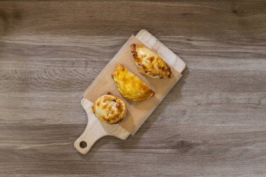 Parşömen kağıdının üzerine tahta bir kesme tahtasının üzerine çıtır çıtır kabuklu üç altın sarısı börek. Rustik tahta tablo arkaplanı, tepeden tırnağa görünüm, kopyalama alanı ile basit bir sunum.