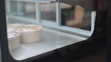 Şefin eldivenli elleriyle taze hazırlanmış çilek, krema ve çikolatalı tatlıları sağlıklı servis dükkanında dondurulmuş vitrine yerleştirirken yakın plan. Müşteri hizmetlerinden önce yemek hazırlama aşamasının son adımı