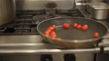 Sıcak tavada yanan vişneli domateslerin yakın çekimi. Profesyonel bir mutfakta yoğun yemek pişirme anı. Yemek hazırlama, yemek tarifi veya restoran içeriği için ideal.
