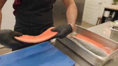 Bir şefin birkaç tepsiden bir tane somon filetosu seçip sonra da çivi kemiklerini özenle çıkardığı yakın plan. Kemikler bir bardak suya girer. Küçük bir mutfak hazırlığı. 4k video
