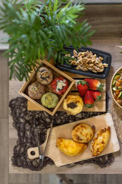 Çeşit çeşit kurabiyeler, börekler, fındıklar ve çilekler kırsal ahşap bir masa ve yeşil bitkiler üzerinde sıralanmış. Ön planda doğal bir bitki olan dikey görüntü. Kopyalama alanı.