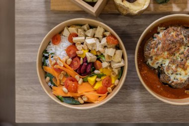 Beyaz pirinç, tofu küpleri, kiraz domatesleri ve doğranmış havuçla servis edilen renkli bir sebze kasesinin yukarıdan görünüşü. Plastiksiz ambalajla dengeli ve hayat dolu bir yiyecek..