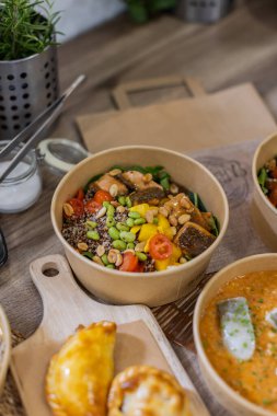 Somon küpleri, kinoa, kiraz domatesleri, mango, edamame ve fıstıklı dürtme kabının dikey yakın çekimi tahtadan bir yüzey üzerinde Kraft kasesinde servis edilir. Sağlıklı yemek hazırlama konsepti, sürdürülebilirliğe odaklı.