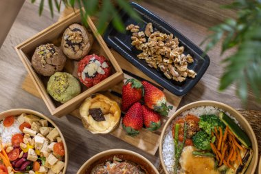 Renkli yemek düzenlemelerinin üst görüntüsü, çeşitli tatlılar. Tahta kutuda zanaatkar kurabiyeleri, çilek, cheesecake, siyah ceviz tepsisi. Ahşap bir yüzeyde canlı bir tonla dikkatlice şekillendirilmiş..