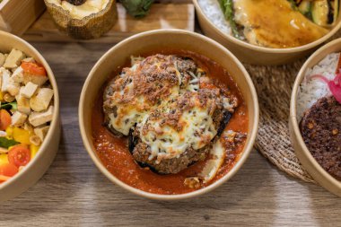 Erimiş peynirle kaplı fırında pişirilmiş patlıcan dolu bir kase dolusu zengin domates sosu. Çevre dostu bir konteynırda hizmet vermiş. Ahşap yüzeyde yatay. Sanatsal servis tabağı, gübrelenebilir gıda kutusu..