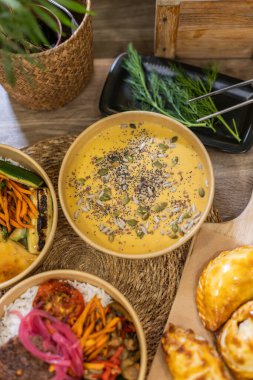 Kraft kasesinde sunulan kabak çorbası, ayçiçeği, susam ve kabak çekirdeği ile kaplı. Etrafı empanadalarla ve taze otlarla çevrili. Sanatsal servis tabağı, gübrelenebilir gıda kutusu. Dikey, kopyala