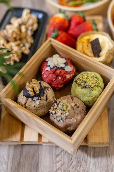 Kare tahta bir kutuda badem, ceviz ve şam fıstığı gibi çeşitli malzemelerle sergilenen beş zanaatkar kurabiye. Dikey yakın plan görüntü, doğal ışıklandırma, yüzeysel alan derinliği.