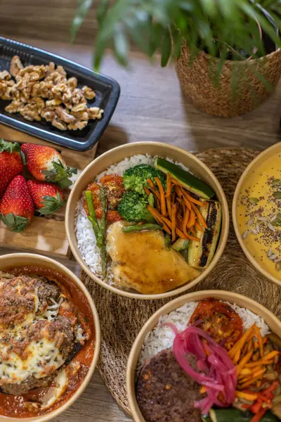 Izgara tavuk, buğulanmış pirinç ve çeşitli sebzelerle dolu servis kasesinin dikey yakın çekimi. Tahta masadaki Kraft konteynırı. Yeni yapılmış sağlıklı yemekler, biyolojik olarak ayrıştırılabilir konteynırlara doldurulmuş..