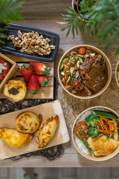 Empanada, çilek, fındık, tatlı ve sebze ve etle dolu sağlıklı kaseler. Kırsal yüzeylerde, ahşap tahtalarda ve yeşillikte sunuluyor. Dikey resim, kopyalama alanı.