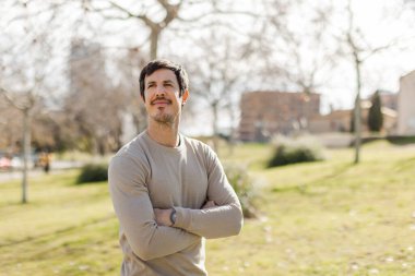 Güneşli bir günde kollarını kavuşturmuş gülümseyen bir adam yukarı bakıyor. Umudu, güveni, iyimserliği gösterir. Kişisel gelişim, kariyer, başarı kavramları için idealdir. Yatay, kopyalama alanı sağda.