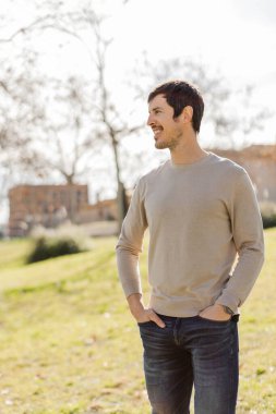 Dışarıda yürürken elleri ceplerinde gülümseyen bir adam. Kolaylık, neşe, güven, yaşam tarzı, refah, pozitiflik ve özgürlük kavramları için harika. Dikey, yumuşak ışık, doğal ortam. Kopyalama alanı