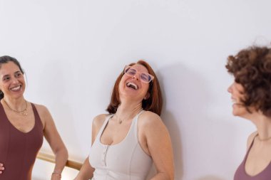 Üç kadının spor salonunda birlikte güldüğü neşeli bir an. Doğal ışık, minimalist alan ve güçlü duygusal bağ. Yaşam tarzı, sağlık ve pilates eğitim ortamı. Yatay