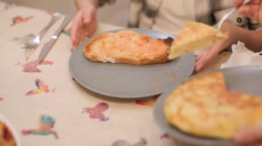 Tabağında domatesli ekmekle bekleyen çocuğuna bir dilim İspanyol omleti servis eden bir kadının detaylı fotoğrafı. Geleneksel ev yemeği, tanınmaz halde. Yatay, 4K