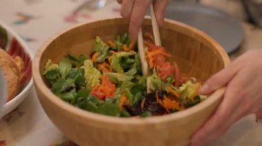 Ev mutfağında aile tabağına taze salata servis etmek için maşa kullanan el resimleri. Sağlıklı Akdeniz yemekleri ve günlük ev işleri. Yatay, 4K