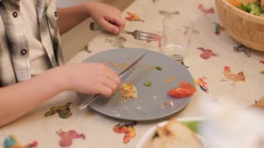 Çocuk bir elin sandalyeyi iterken ve yemeği bitirdikten sonra yemek masasından boş bir tabak alırken çekilmiş ayrıntılı bir fotoğraf. Günlük rutin ve sorumluluk duygusu. Yatay, 4K