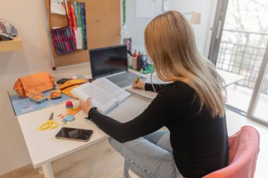 Genç kız renkli bir yatak odasında derslerine odaklanmış, okurken bir deftere yazıyor. Etrafı okul malzemeleriyle çevrili, rahat ve renkli bir yatak odasında. Yumuşak ışın. Yatay, yüksek açı görünümü