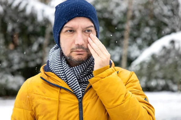 Young man having itching eyes health problem. Sick man in winter snow touching her sensitive ey