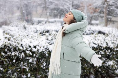 Genç gülümseyen kadın şehirde kışın karlı gününün tadını çıkarıyor.