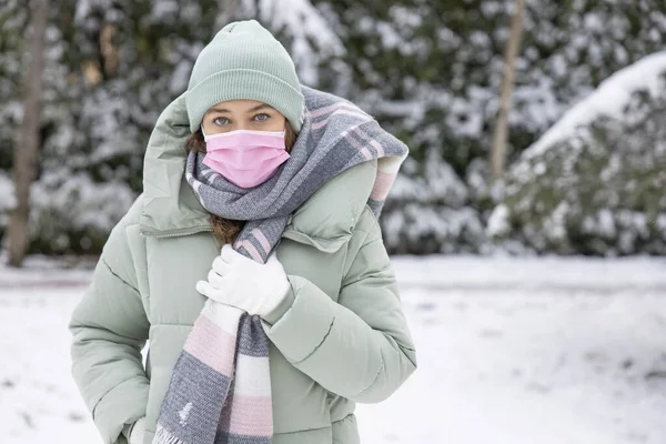 Young woman with protective face mask on a snowy day