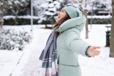 Genç gülümseyen kadın şehirde kışın karlı gününün tadını çıkarıyor.
