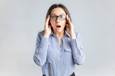 Surprised young businesswoman in eyeglasses standing in front of gray background 