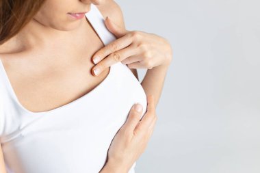 Young woman doing breast self-examination on gray studio backgroun