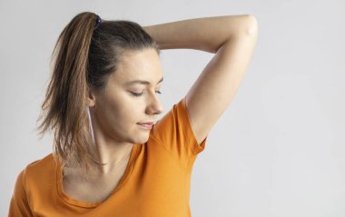 Young woman smelling her underarms in studio gray backgroun