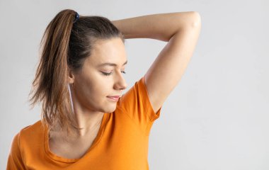 Young woman smelling her underarms in studio gray backgroun clipart