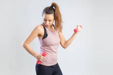 Young sporty woman exercising with dumbbells over gray background