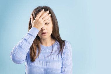 Portrait of upset, sad woman having head ache, stress, troubles, touching head and close eyes, standing over blue background
