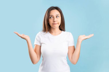 Confused expression young woman with arms and hands raised on blue background. Doubt concept