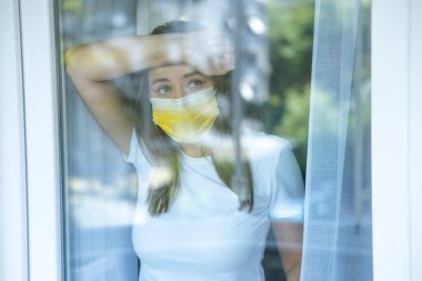 Young woman who cannot leave the house in quarantine due to an epidemic Covid-19 and looking through the window