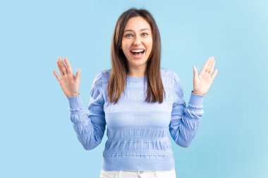 Close up portrait of amazed woman gesturing shock, extremely happy, with wide open eyes, shouts isolated on blue background.