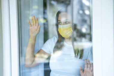 Young woman who cannot leave the house in quarantine due to an epidemic Covid-19 and looking through the window