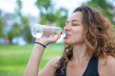 Young woman drinking water from bottle while sitting in the park