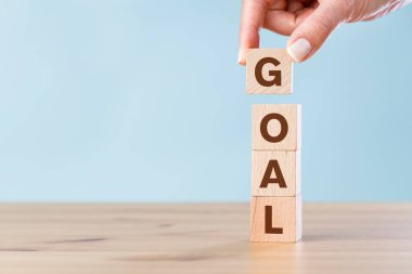 Woman hand arranging wooden cubes with GOAL word. Business success goal concept.