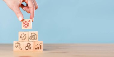 Kadın eli, mavi arka planda ikon olan tahta küp bloğu yığıyor. İş stratejisi ve eylem planı kavramı