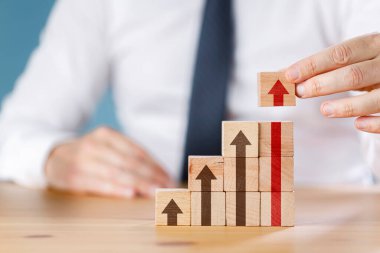 İşadamı tahta blokları ok sembollü merdiven olarak düzenliyor. Ekonomik, mali veya kariyer büyümesi, kalkınma veya progres