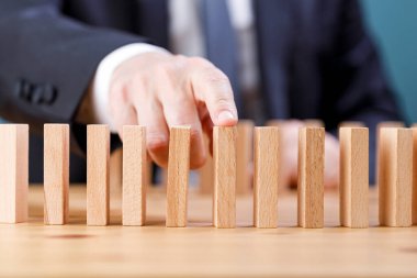 İşadamı, tahta bloğun risk kavramı ile domino hattına düşmesini engelliyor.