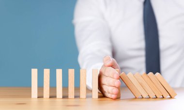 İşadamı eli, tahta domino taşının tahtaya etkisini durdurdu.