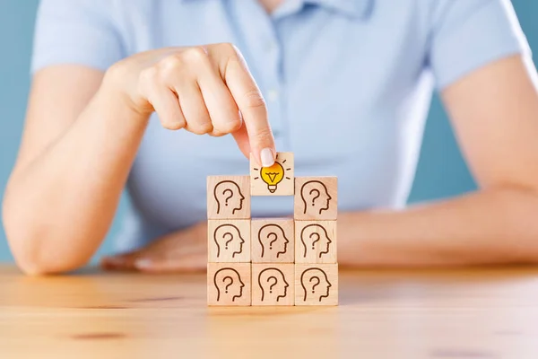 Hand putting wooden cube block which print screen lightbulb icon on human head with questions mark. Creative idea and innovation.