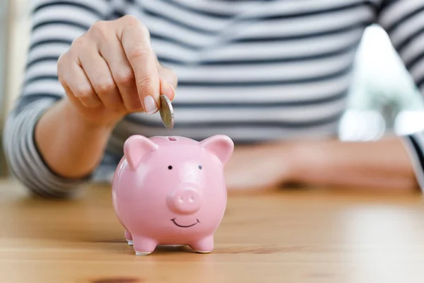 Woman hand putting money into piggy bank. Concept of money saving and budgeting. Saving money with pink cute piggy bank