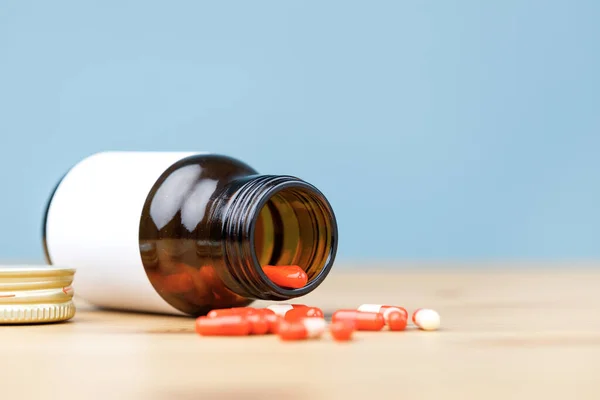 Medicine bottle and red pills on wooden table. The pills spill onto a wooden table.