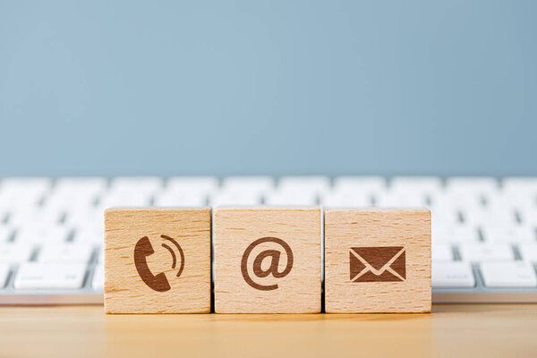 Communication icons on wooden cube blocks and in front of a keyboard. Contact us or e-mail marketing concept 