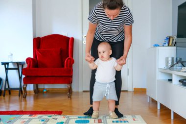 Anne, bebeğine evde ilk adımlarını atması için yardım ediyor.