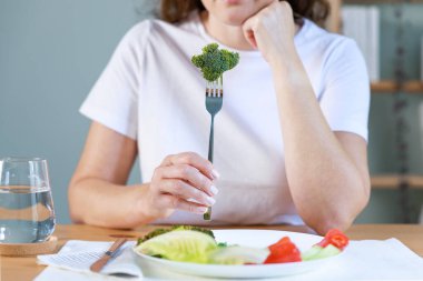 Diyetin ilk günü. Brokolide salata tabağında çatal tutan mutsuz genç bir kadın taze sebze yemekten hoşlanmıyor.