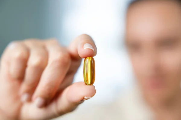 Woman holding yellow soft gel vitamin capsule