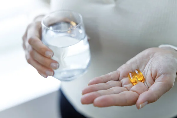 Close up of woman holding vitamin capsules and glass of water. Nutritional Supplements. Capsules vitamin and dietary supplements
